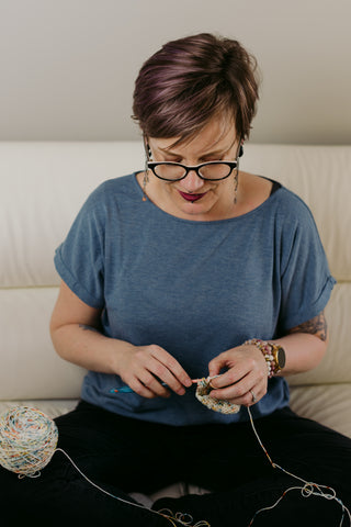 Femme assise fait du crochet. Elle porte un t-shirt bleu.