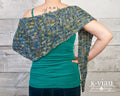 Adstock Tunisian Crochet Shawl Pattern worn by woman with her back turned against a wood slat wall.