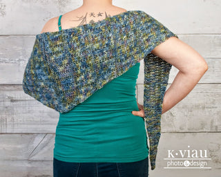 Adstock Tunisian Crochet Shawl Pattern worn by woman with her back turned against a wood slat wall.