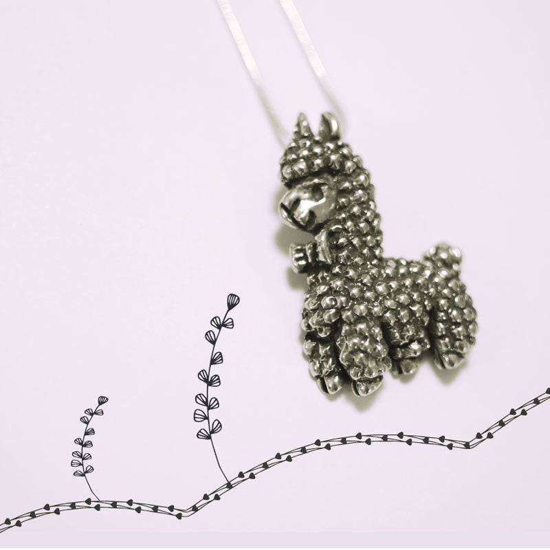 Alpaca pewter pendant on white background with line drawings of flowers.