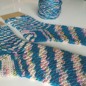 Blue and white crashing waves crochet socks on white background with yarn ball in the back.