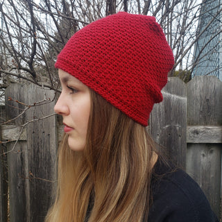 Red crossed-seams crochet hat worn by teenager in front of a fence.