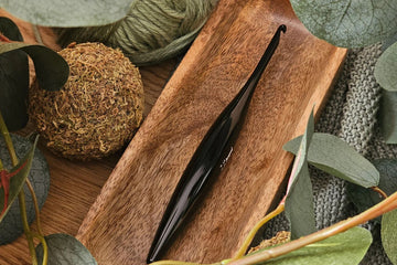 Furls_Metal_Onyx_Crochet_Hook in wooden tray with leaves and blanket flatlay.