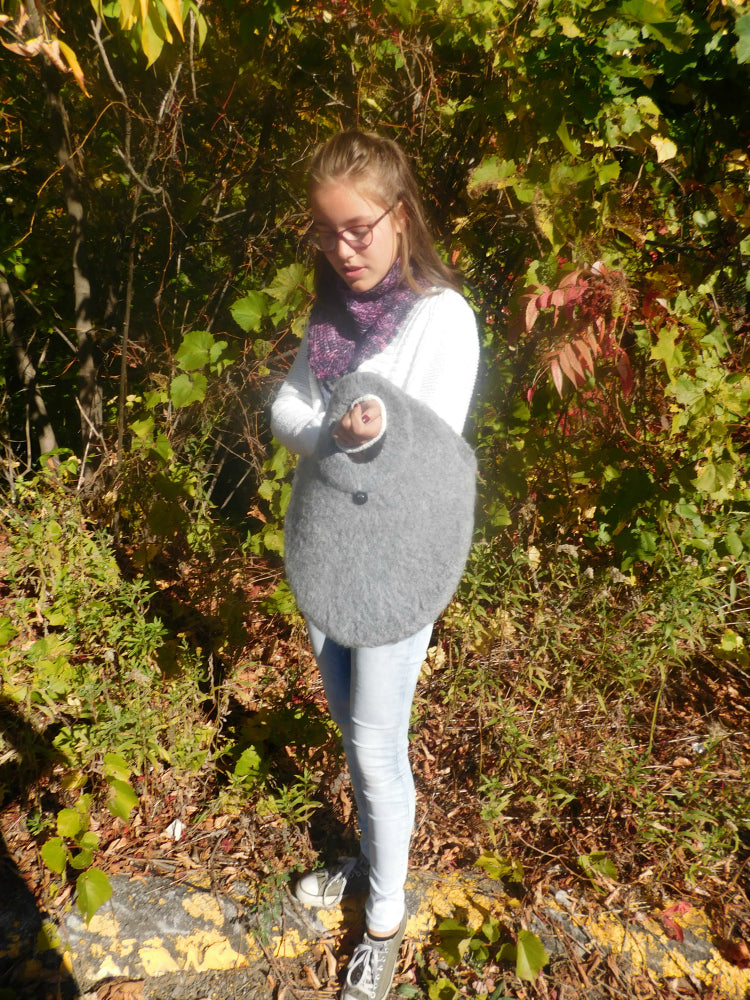 Gray Ricochet-felted-crochet-bag held by young woman outside.
