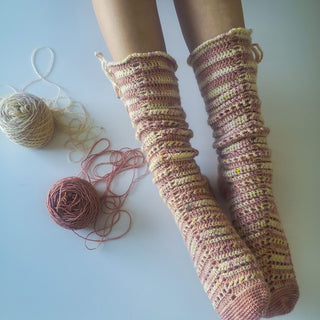 Romance Crochet Socks worn against white background with 2 balls of yarn on the side.