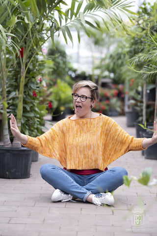 Sunset Boulevard Tunisian Crochet Pattern worn by woman sitting cross-legged in a plant shop.