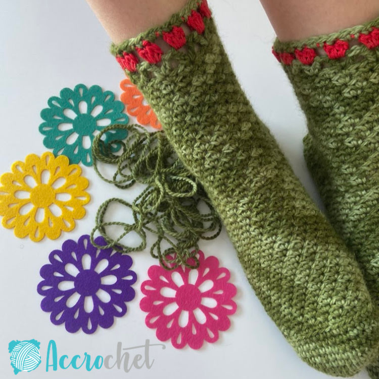 Tulip-slipper-socks on feet with flower coasters and yarn on white background.
