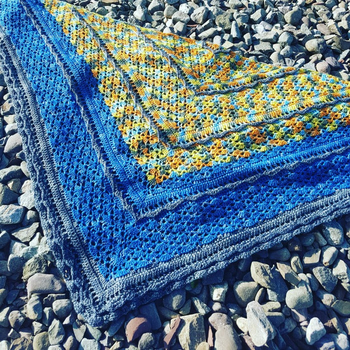 Blue and yellow Un-air-de-fleuve-crochet shawl on rocks.