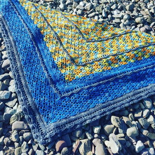 Blue and yellow Un-air-de-fleuve-crochet shawl on rocks.