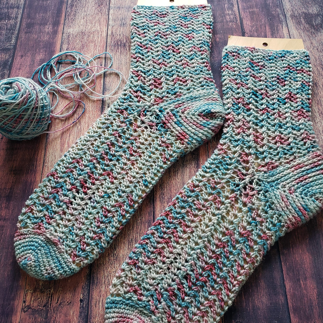 Unicorn-Dream crochet socks on blockers against dark wood background.