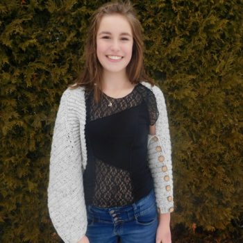 Oatmeal convertible crochet top worn by young woman in front of cedars.