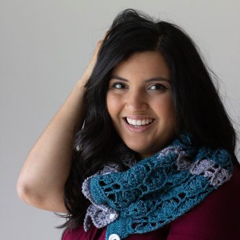 Woman with purple t-shirt wearing teal and gray crochet cowl