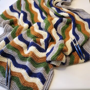 Crochet chevron striped throw with 4 crochet hooks laying on top in groups of 2