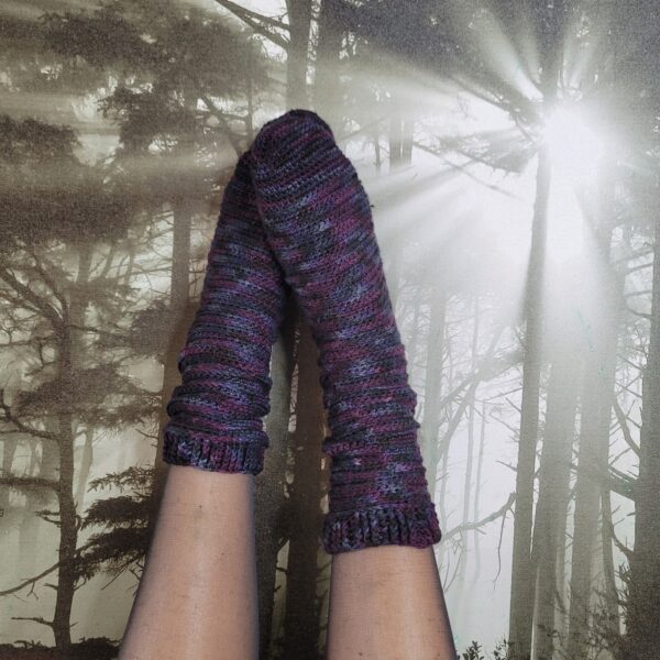 Grape Jelly crochet socks worn and resting on a picture of dark trees