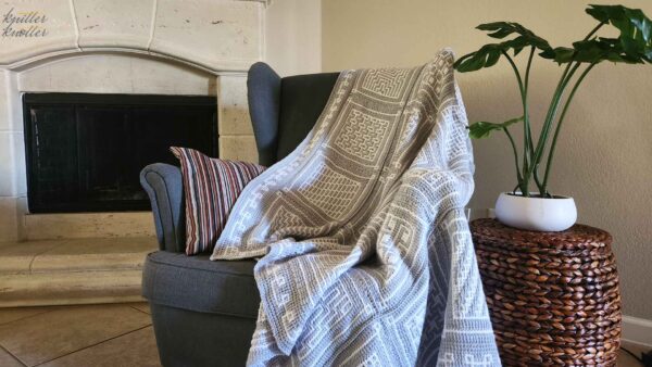 Tunisian crochet Blanket laying on a couch with a fireplace to the left, and a side table and plant to the right