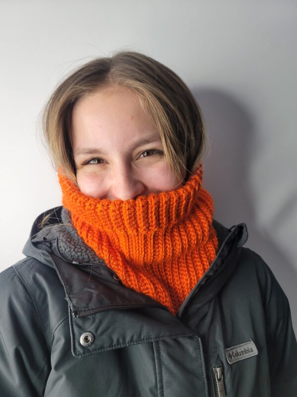 Orange Campfire winter hood worn as a cowl under a black winter coat by smiling young woman